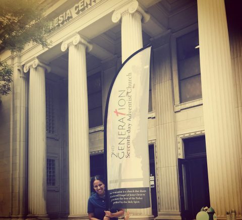 Woman standing nest to a banner that reads 'Second Generation Seventh-day Adventist Church